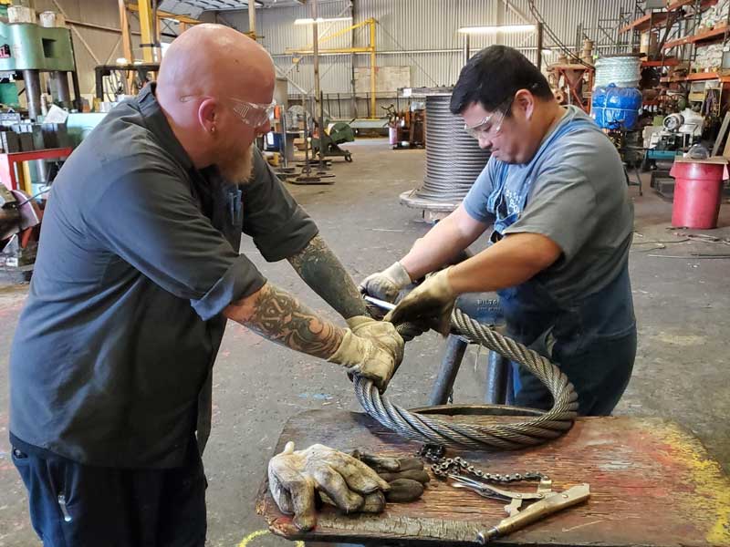 Two men wearing safety glasses bending a wire rope